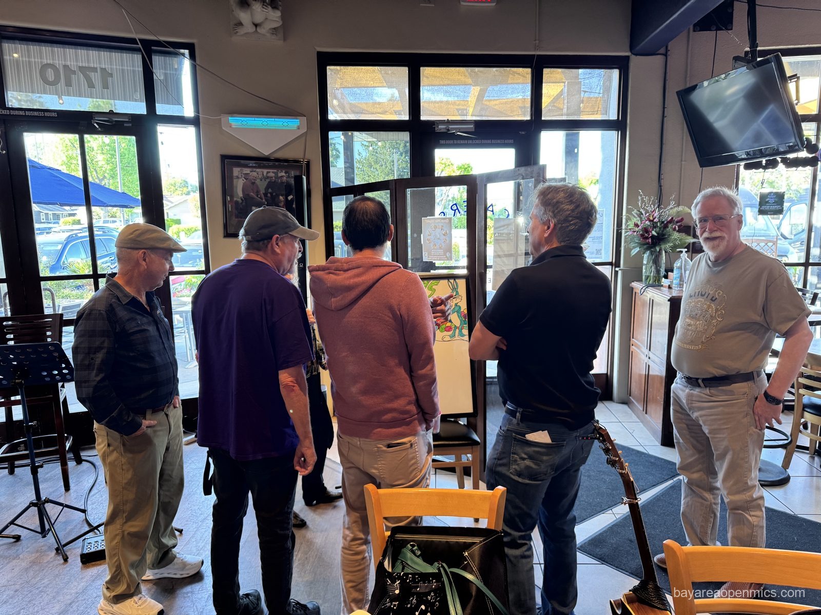 six men stand with their backs to the camera in front of a white board