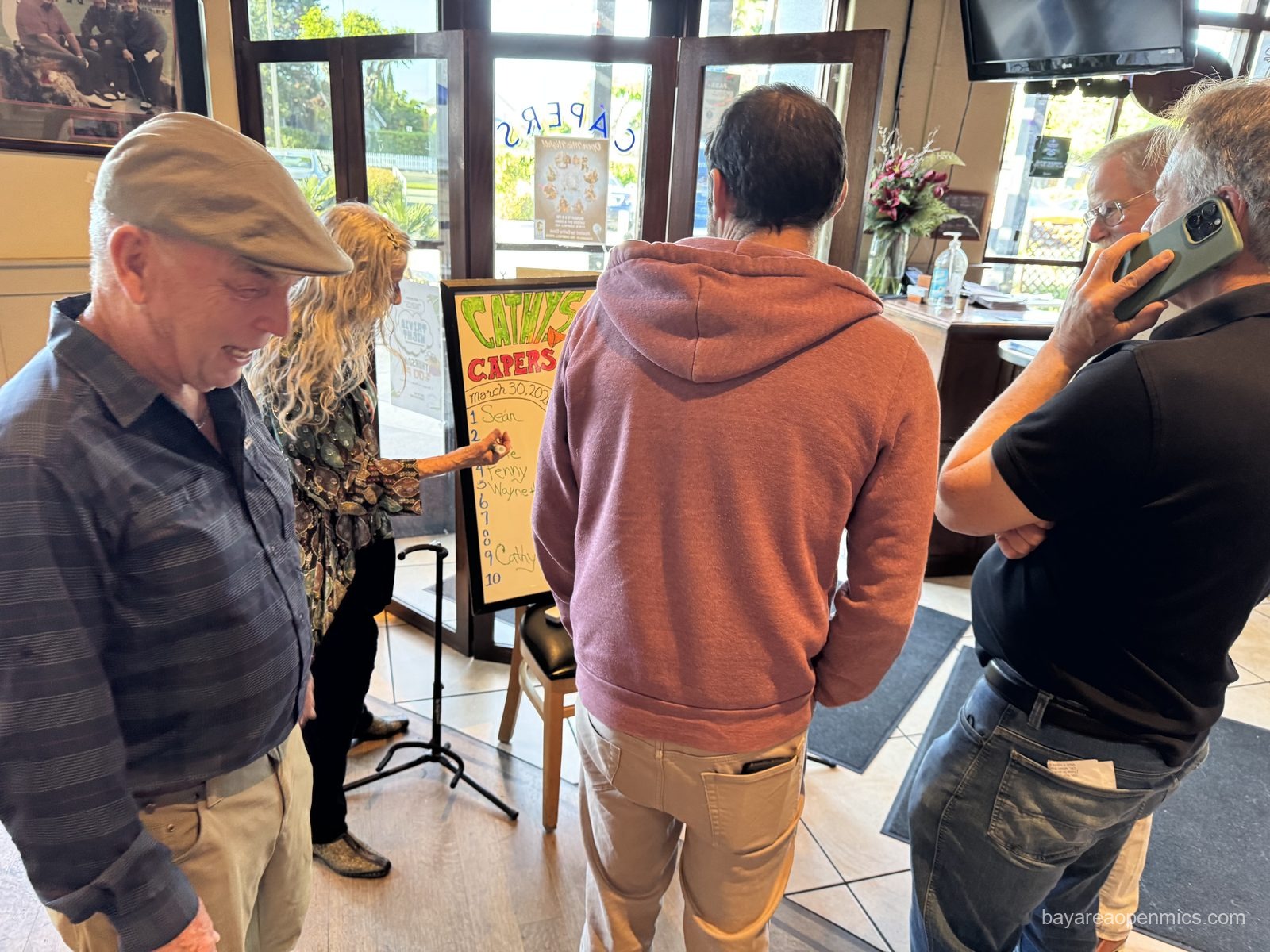 a man in a crowd around a sign up sheet holds a phone to his ear