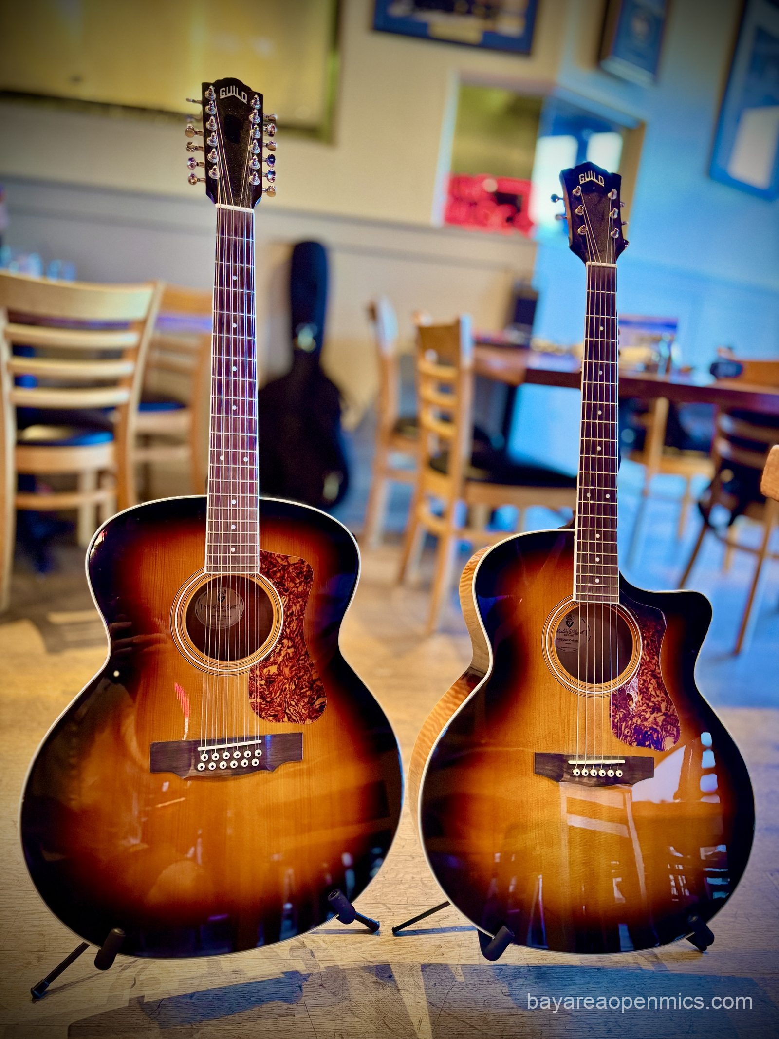 a pair of beautiful sunset burst Guild guitars, a matching 12-string and 6-string, sit beside each other, their veneers gleaming like polished glass