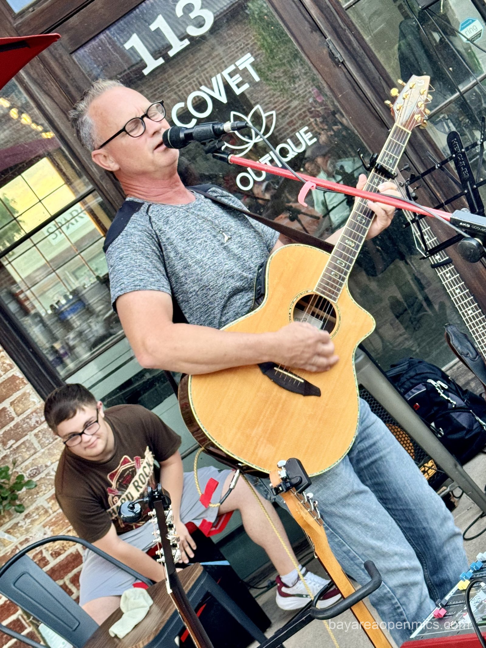 a young man joyfully plays a cajon behind an older man playing guitar and singing