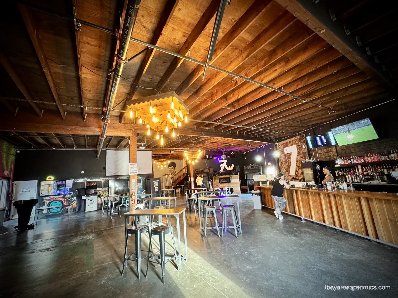The cavernous warehouse interior of 7th West in Oakland, with high-top stools and a long bar