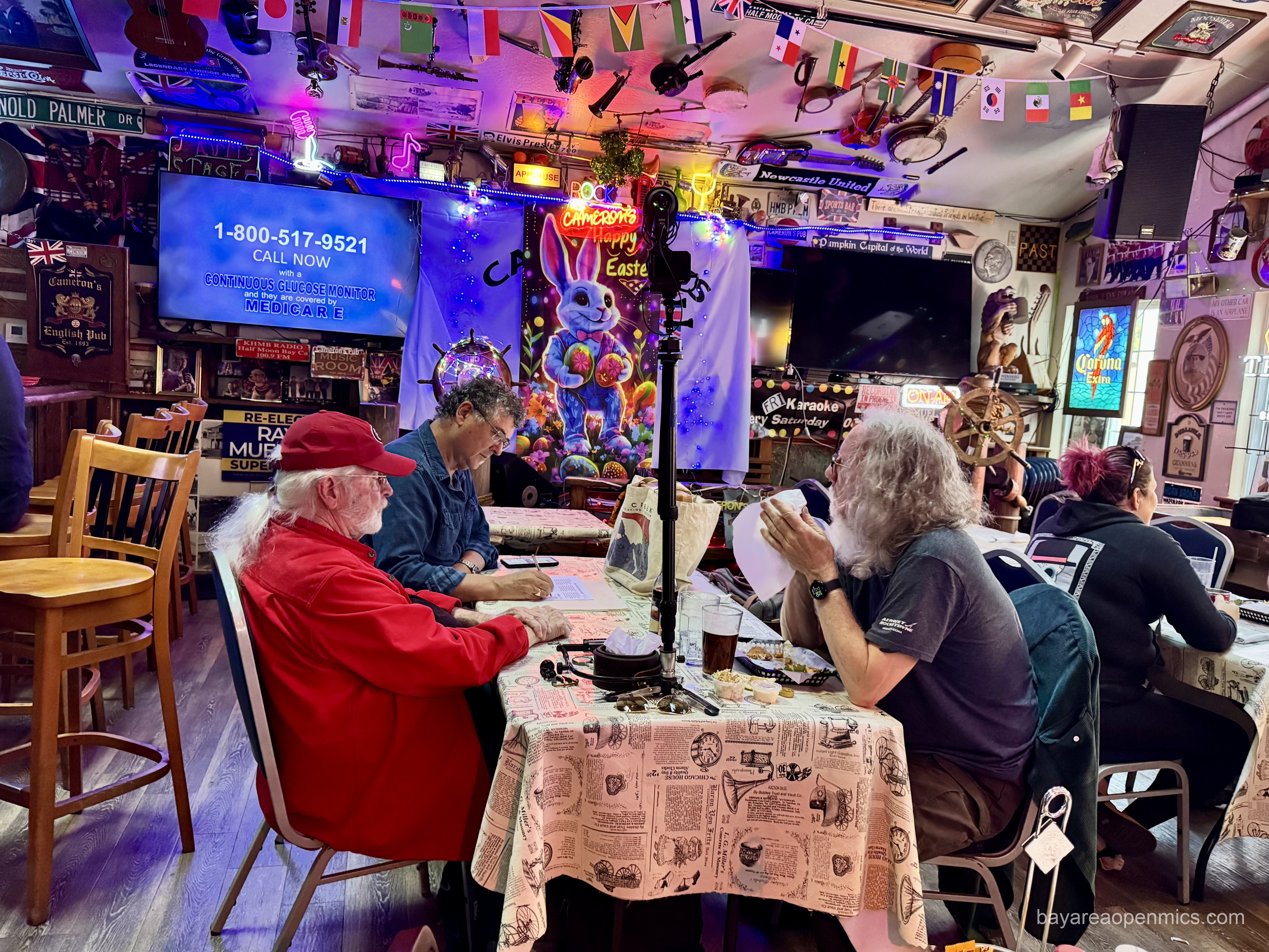 Three men sit at a table in front of a stage set up for music