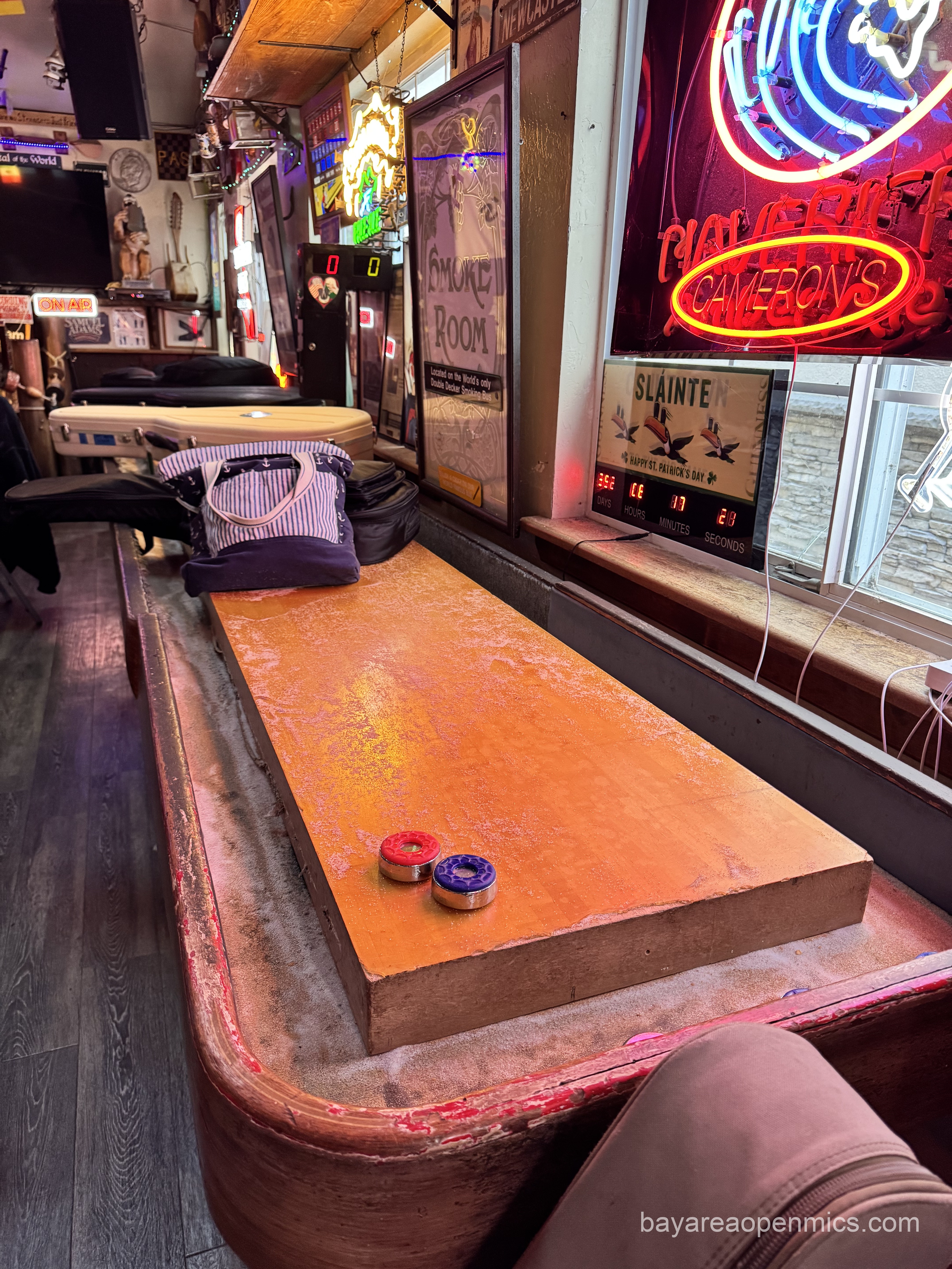 A shuffleboard table with two pucks and a few guitar cases