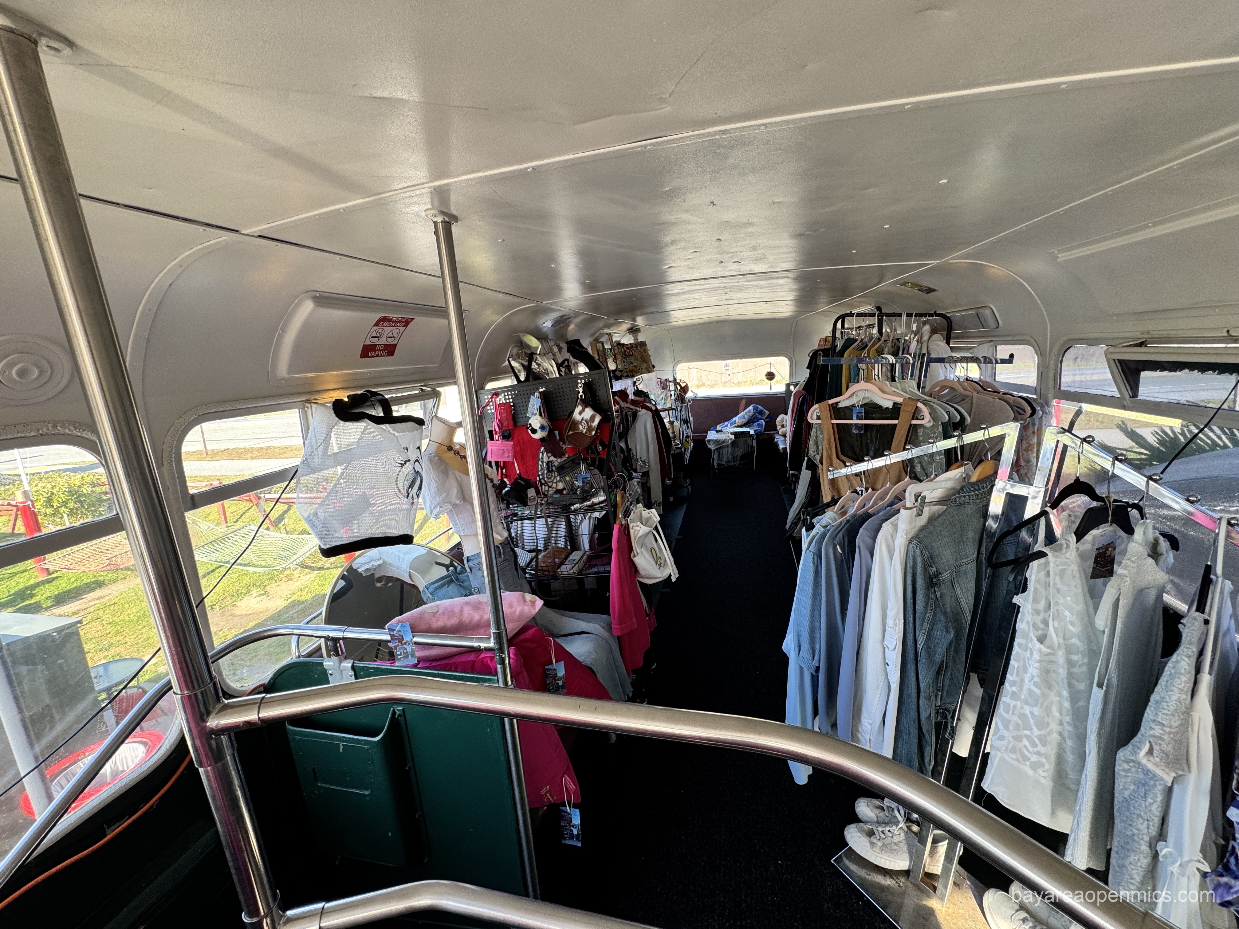 A collection of hanging clothes and knick-knacks for sale under the curved room of the bus