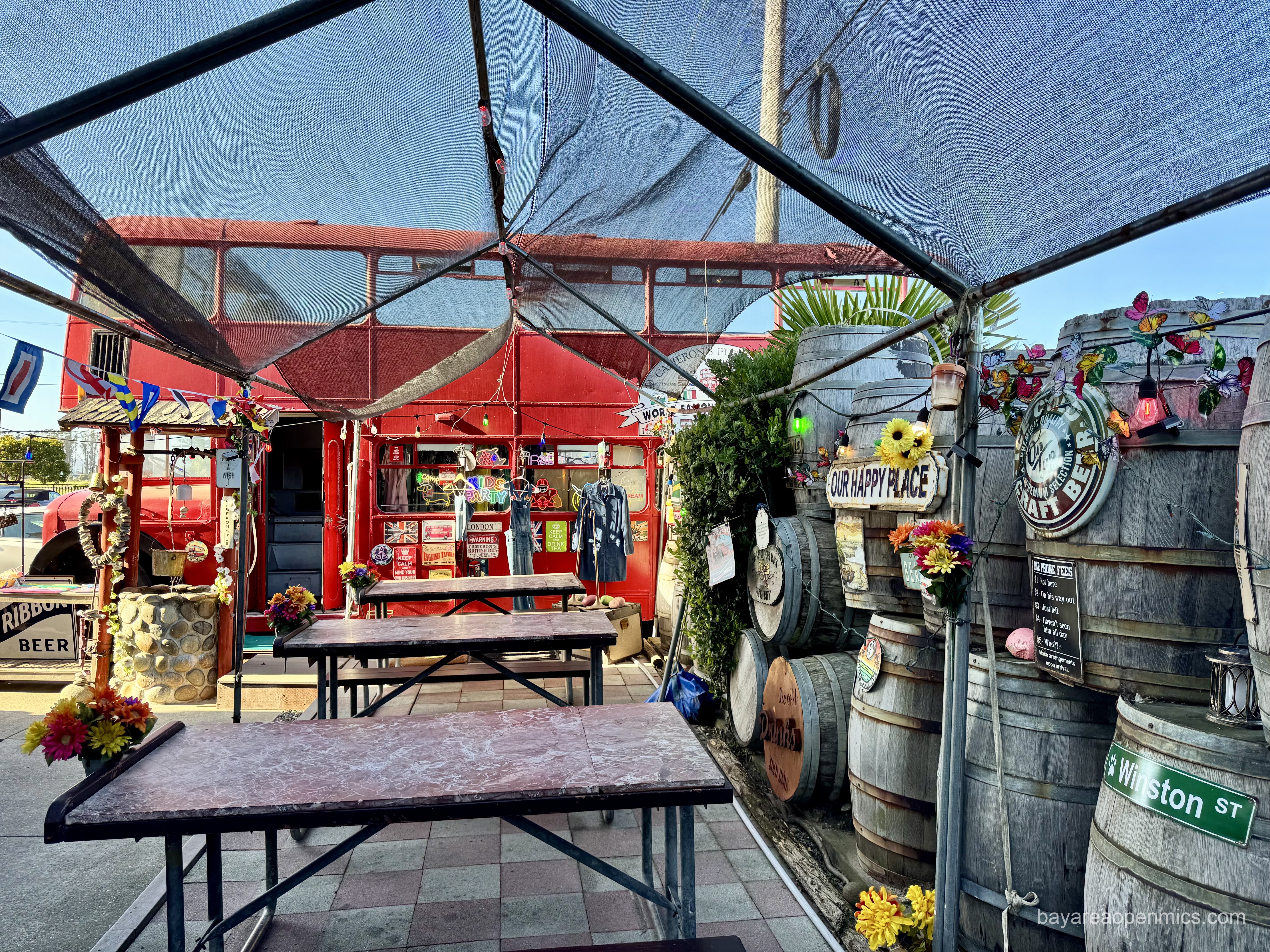Barrels line the wall next to a row of tables with the London double-decker bus in the background