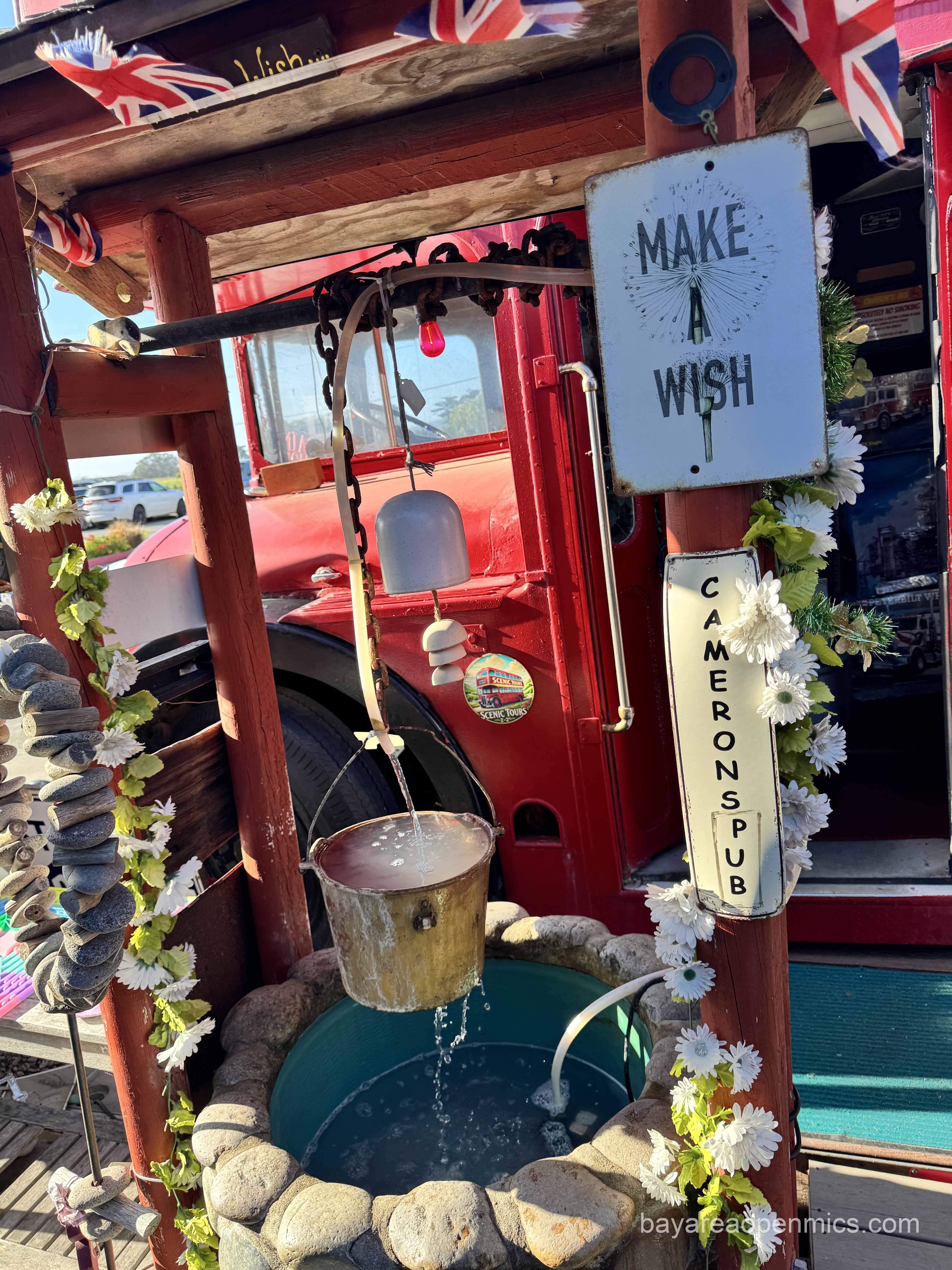 A sign reads, 'Make a Wish' above a bucket with running water over a well outside the double-decker London city bus